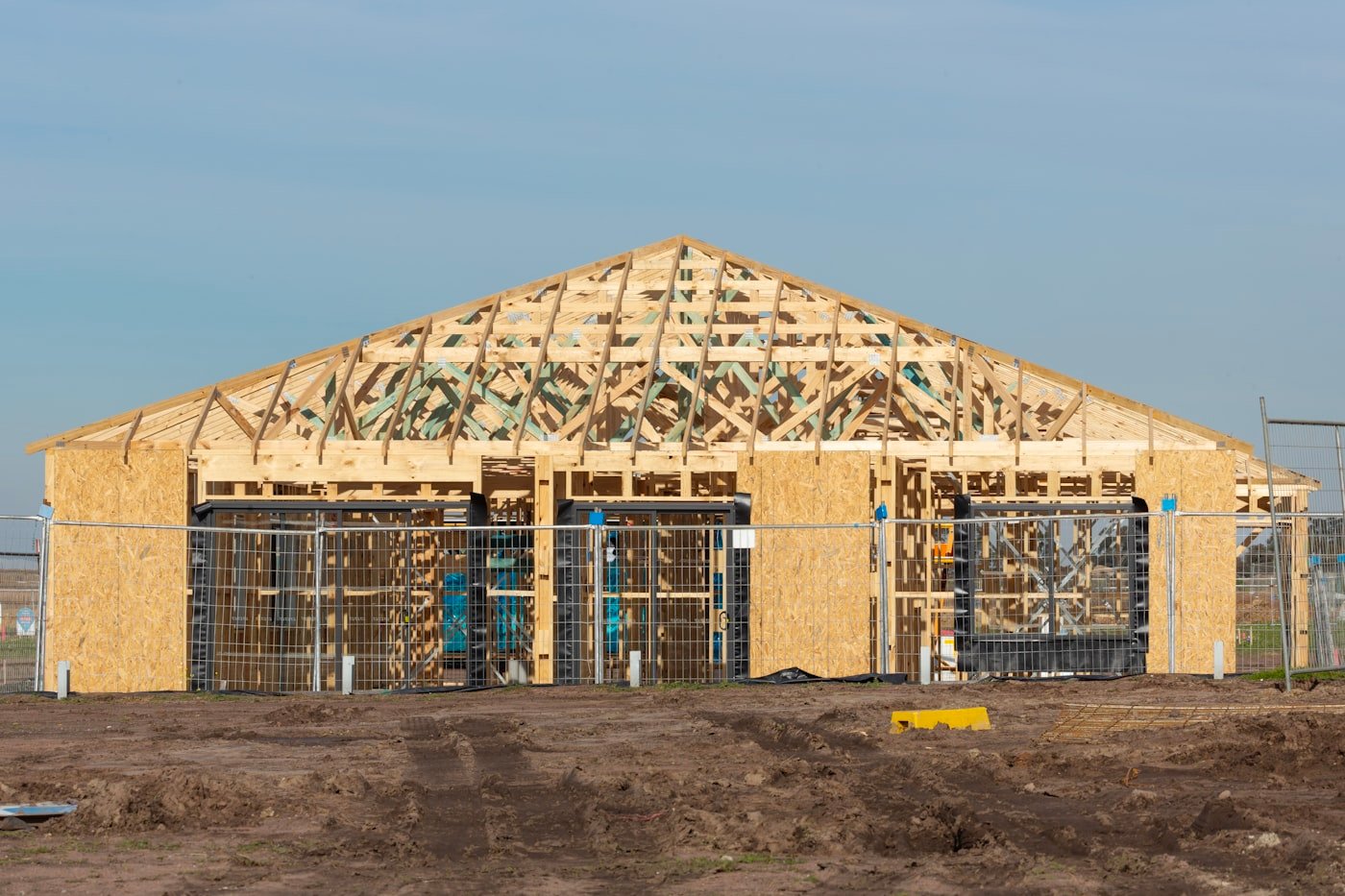 Newly constructed wooden frame house with exposed structure, surrounded by construction fencing, in a South Florida building site.