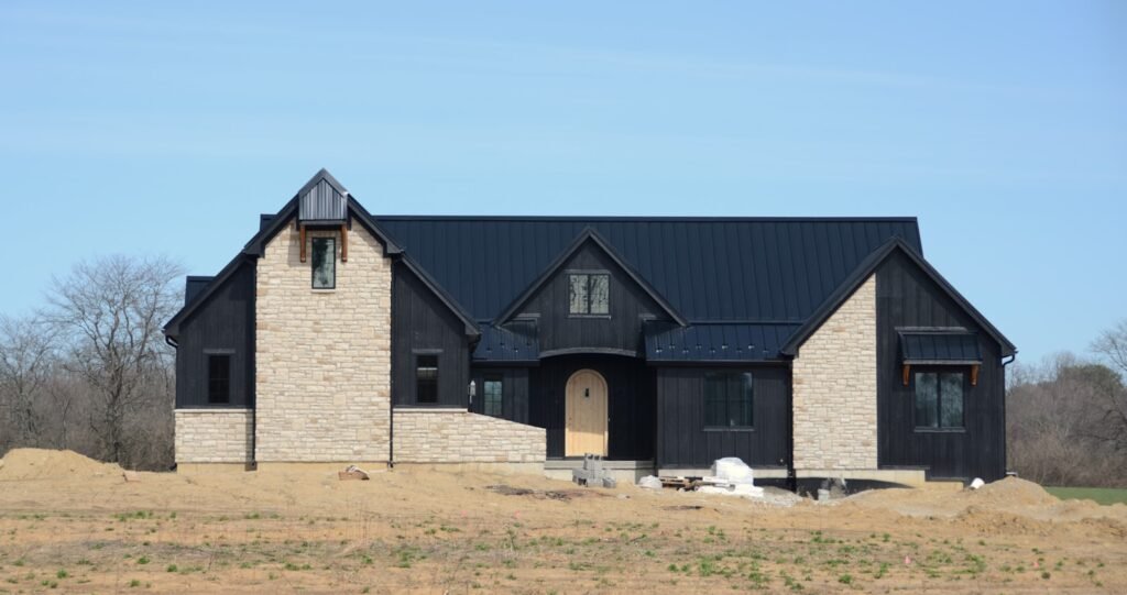Luxury custom home under construction in South Florida, featuring a combination of stone and black siding, set in a rural landscape.